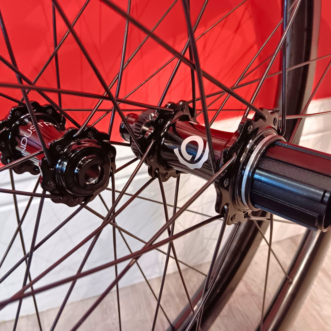 Close-up of a bicycle wheel hub and spokes with a red and black bicycle frame in the background.