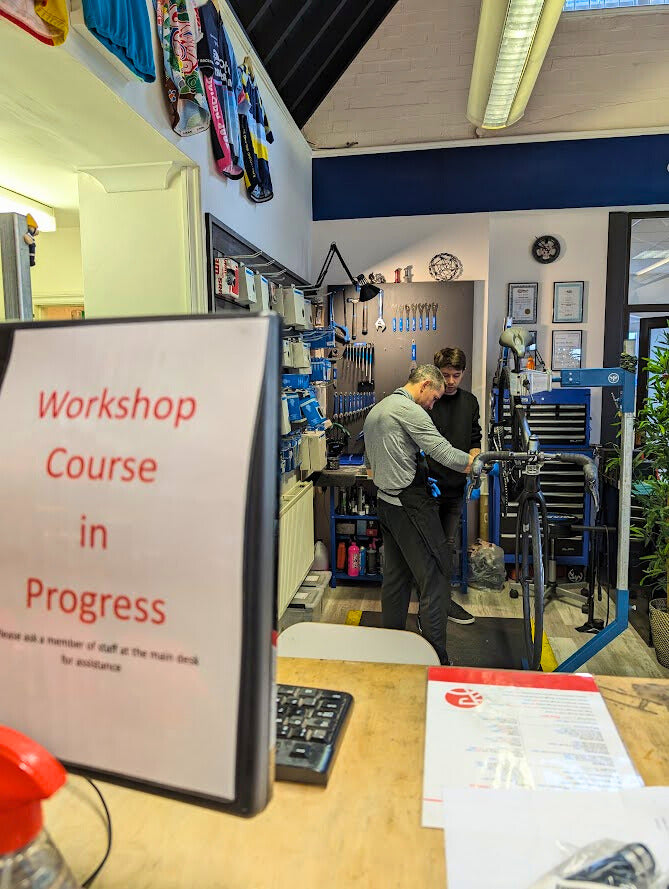 Two people working in a workshop with a 'Workshop Course in Progress' sign.